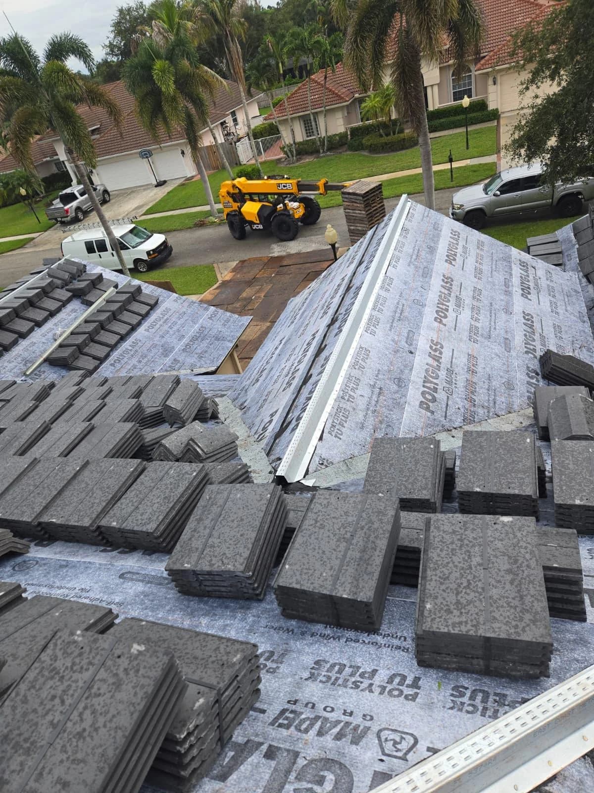 Telehandler beside a plywood-protected driveway during Jupiter rooftop tile loading